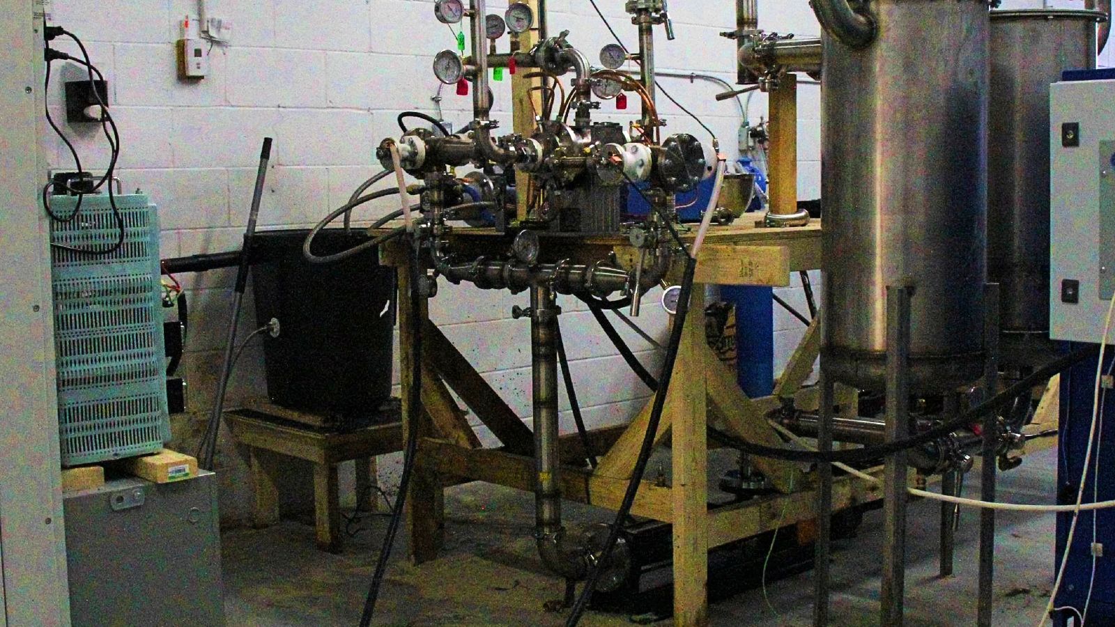 Prototype Four: stainless steel cavitation reactor with pressure gauges and piping on a test bench, with process tanks on the right