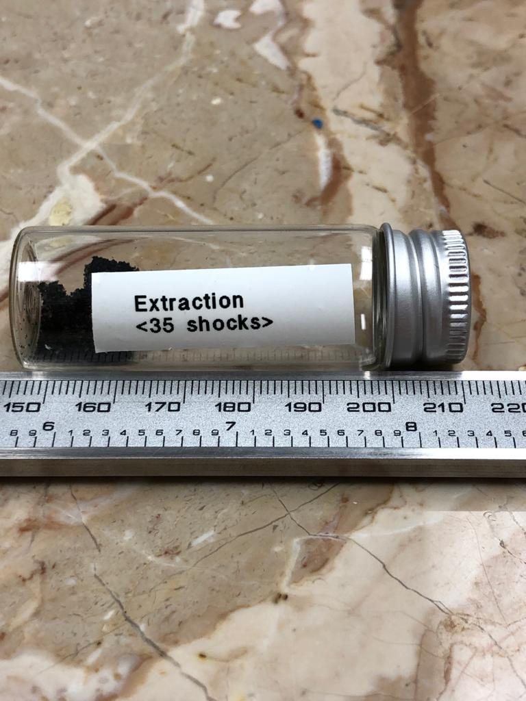 Glass sample vial labelled Extraction 35 shocks, holding dark extracted material, next to a ruler